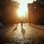 People walking and cycling on a cobblestone street during the golden hour