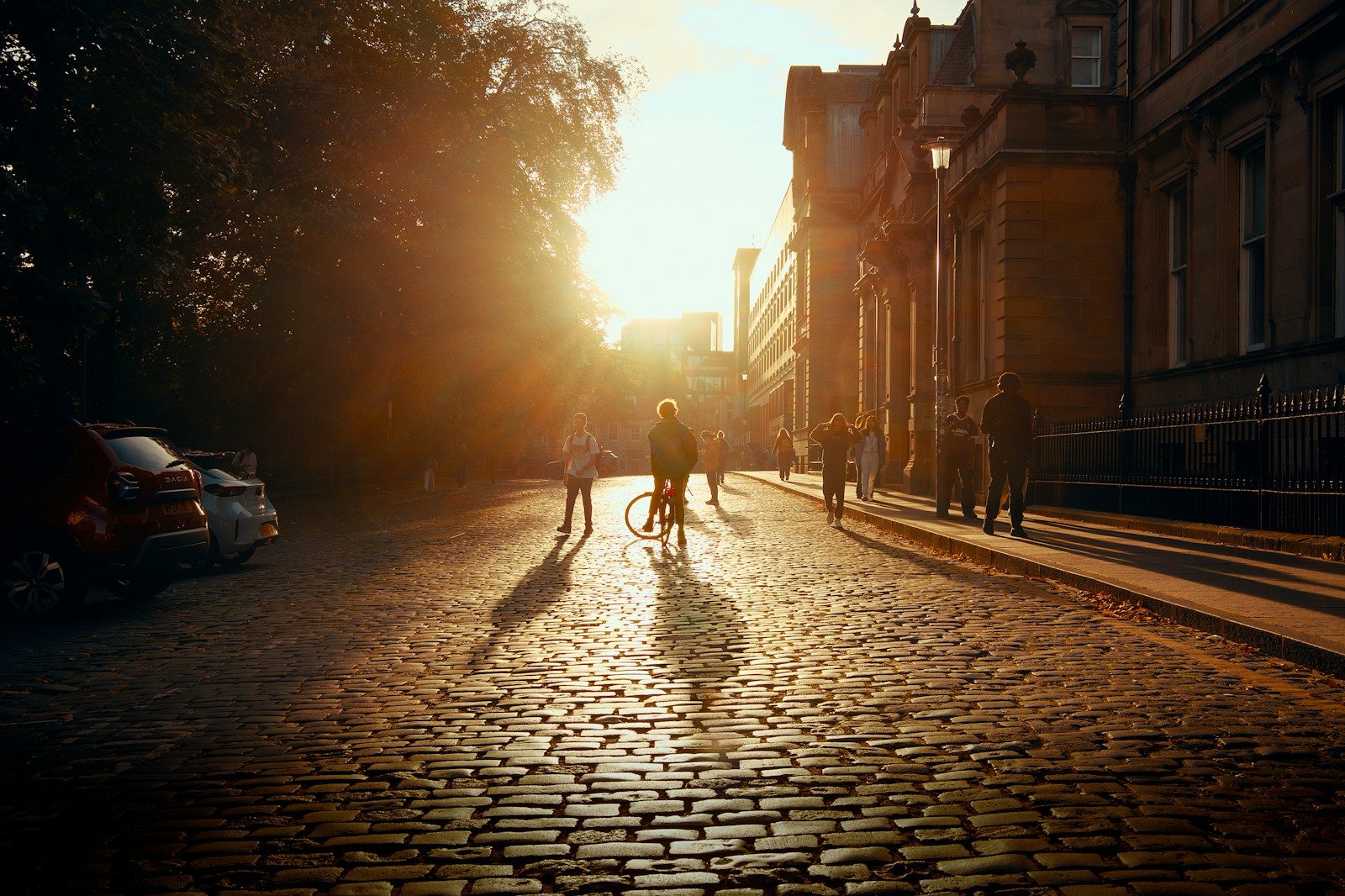 People walking and cycling on a cobblestone street during the golden hour